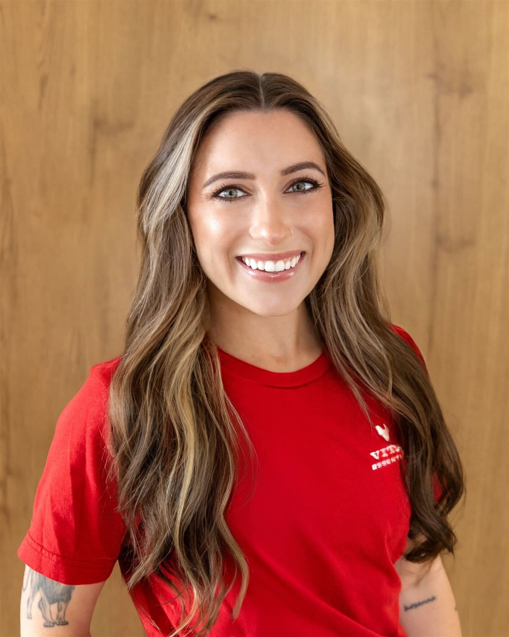 Headshot of Ashlyn in red Vital Essentials shirt against wood background